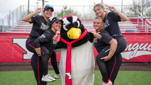 Four members of the YSU softball team pose with YSU's Pete the Penguin mascot on the YSU Softball Field